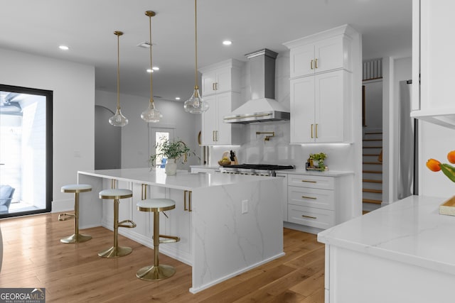 kitchen with light wood-type flooring, white cabinetry, wall chimney exhaust hood, and recessed lighting