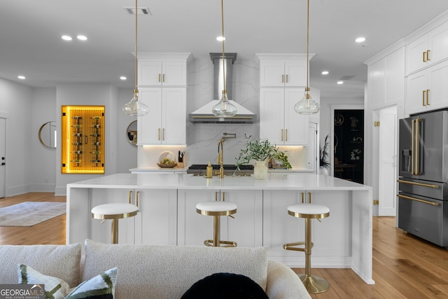 kitchen with wall chimney exhaust hood, high end refrigerator, light countertops, and visible vents