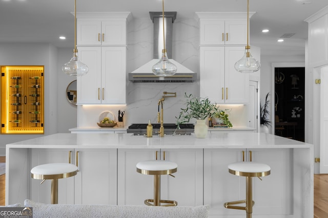 kitchen with a center island with sink, recessed lighting, backsplash, white cabinetry, and wall chimney range hood