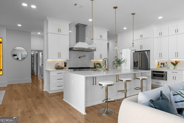 kitchen with light wood finished floors, high end refrigerator, visible vents, wall chimney exhaust hood, and light countertops