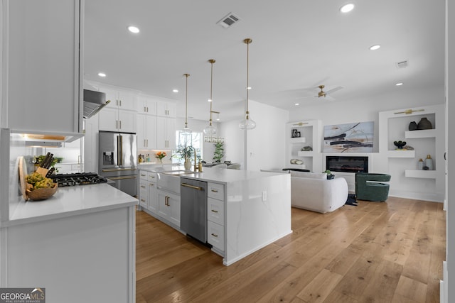 kitchen with stainless steel appliances, visible vents, light wood-style floors, white cabinets, and a glass covered fireplace