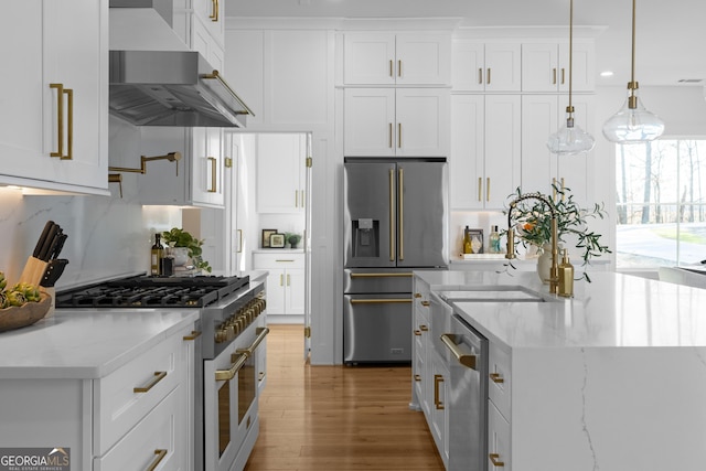 kitchen featuring wall chimney range hood, white cabinetry, high end appliances, and light stone counters