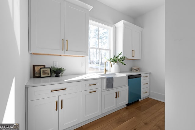 kitchen featuring light countertops, light wood-style flooring, white cabinets, a sink, and dishwasher