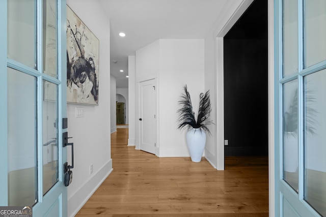 corridor featuring arched walkways, baseboards, light wood-style flooring, and recessed lighting