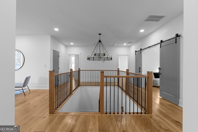 corridor with visible vents, a barn door, hardwood / wood-style flooring, and an upstairs landing