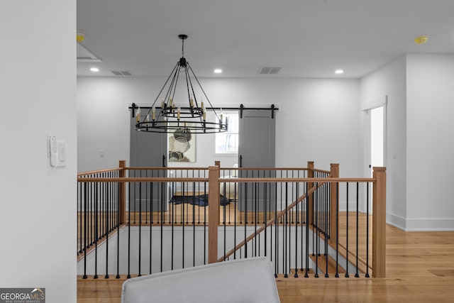 interior space featuring a barn door, recessed lighting, wood finished floors, visible vents, and an upstairs landing