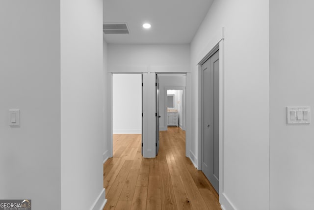 corridor with light wood-style flooring, visible vents, and baseboards