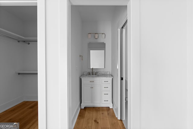 bathroom featuring baseboards, a walk in closet, wood finished floors, and vanity