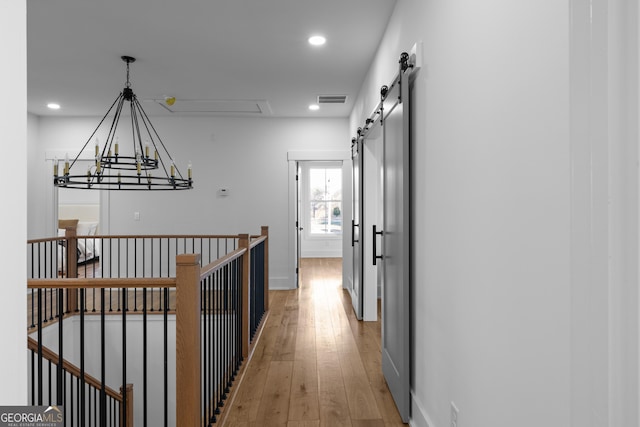 hall with light wood-style floors, recessed lighting, visible vents, and a barn door