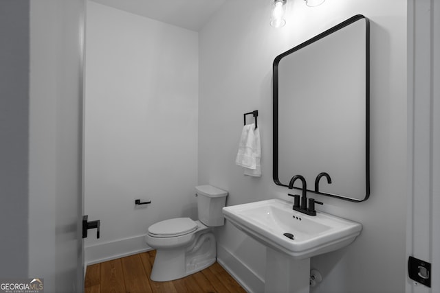 half bath with a sink, wood finished floors, toilet, and baseboards