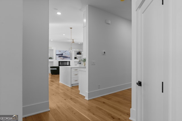 hall featuring light wood finished floors, baseboards, and recessed lighting