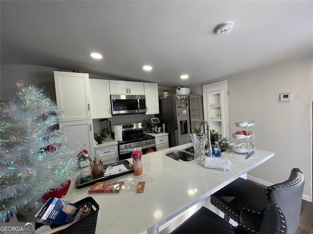 kitchen with a breakfast bar area, stainless steel appliances, a sink, white cabinets, and light countertops