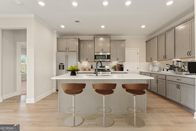 kitchen featuring gray cabinetry, appliances with stainless steel finishes, ornamental molding, a sink, and an island with sink