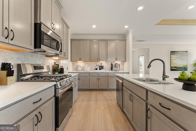 kitchen featuring light wood finished floors, stainless steel appliances, light countertops, backsplash, and a sink