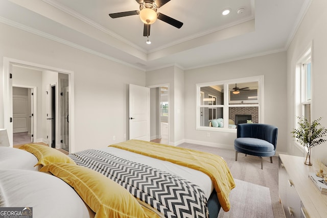 bedroom featuring ornamental molding, a tray ceiling, a fireplace, and light colored carpet