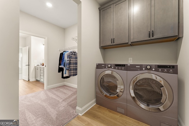 clothes washing area featuring light wood-style flooring, washing machine and clothes dryer, cabinet space, and baseboards