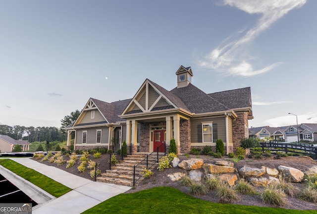 craftsman house featuring stone siding, a shingled roof, and fence