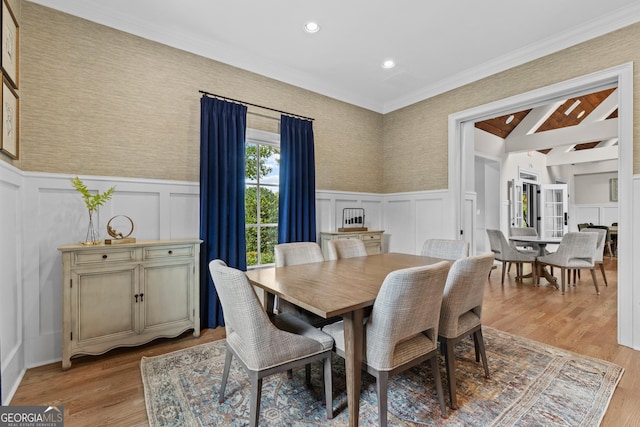 dining space with a wainscoted wall, a decorative wall, crown molding, and light wood-style floors