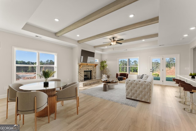 living room featuring light wood finished floors, beamed ceiling, a fireplace, and visible vents