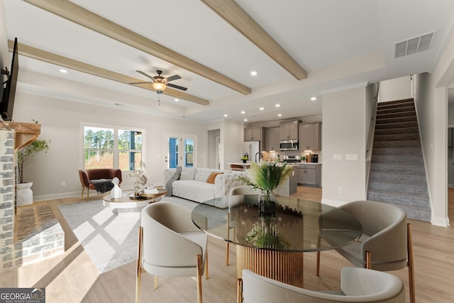 living area featuring light wood finished floors, visible vents, a fireplace with raised hearth, stairway, and beamed ceiling