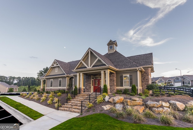 craftsman-style house featuring stone siding, a shingled roof, and fence