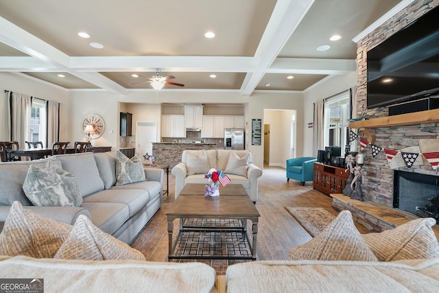 living area featuring a fireplace, coffered ceiling, baseboards, light wood-type flooring, and beam ceiling