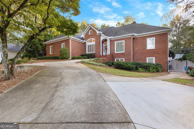 view of front facade featuring concrete driveway, brick siding, fence, and a gate