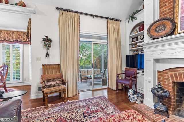 living area with built in features, a brick fireplace, and wood finished floors