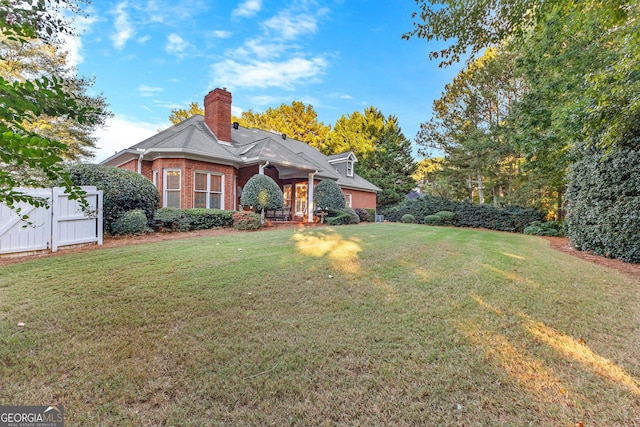 view of front facade with brick siding, a front lawn, a chimney, and a gate