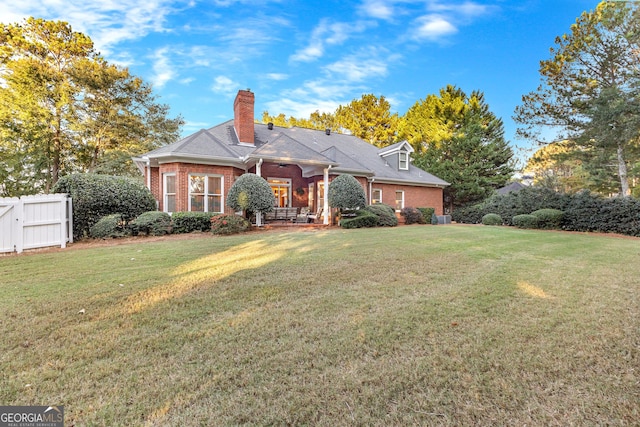 back of house with brick siding, a lawn, a chimney, and fence