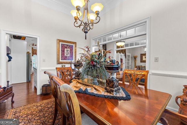 dining area featuring a towering ceiling, a chandelier, wood finished floors, and ornamental molding