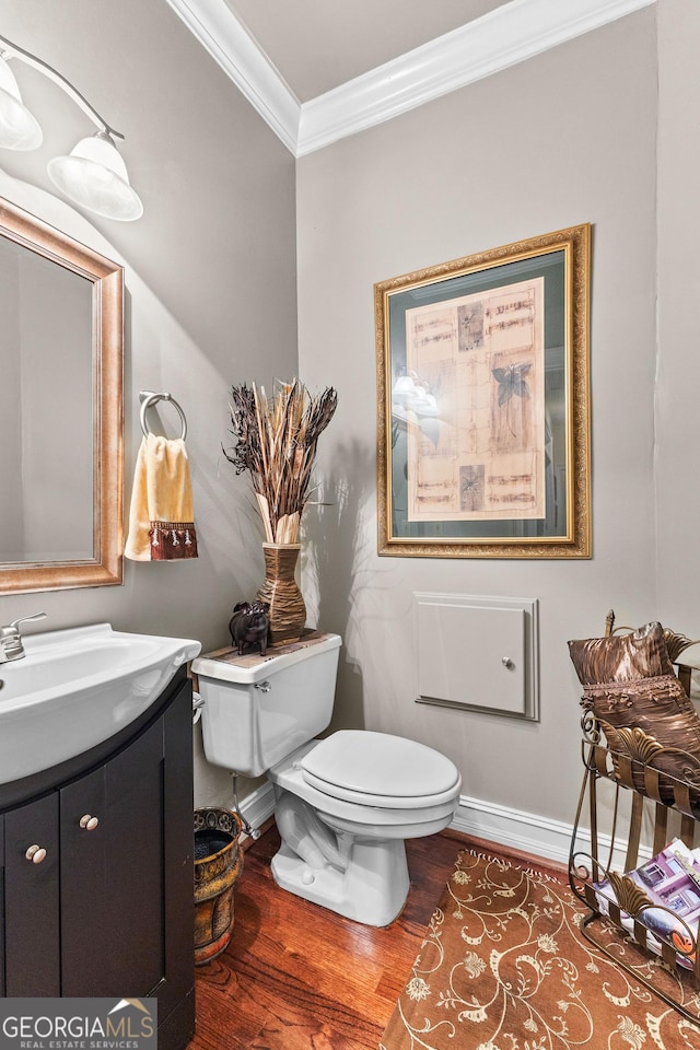 half bath with toilet, ornamental molding, vanity, wood finished floors, and baseboards