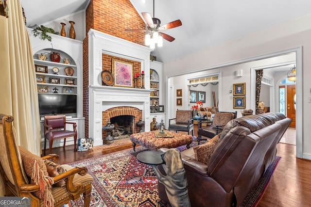 living room with built in features, a fireplace, vaulted ceiling, ceiling fan, and wood finished floors