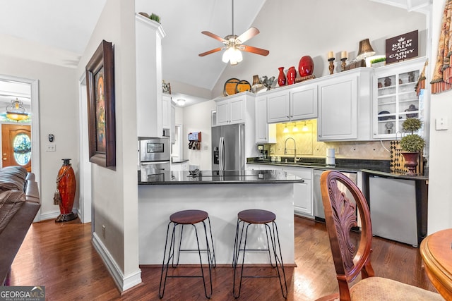 kitchen featuring a breakfast bar, dark wood-style flooring, dark countertops, appliances with stainless steel finishes, and a peninsula