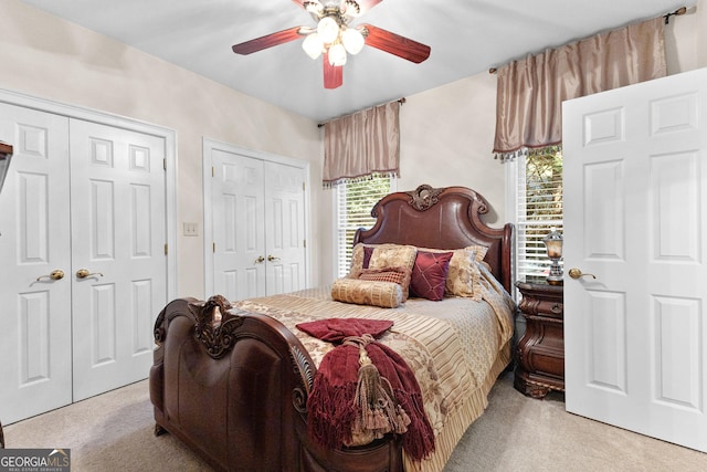 bedroom featuring light carpet, ceiling fan, and two closets