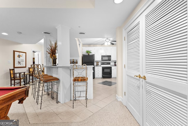 kitchen with a breakfast bar area, visible vents, white cabinets, a peninsula, and black appliances