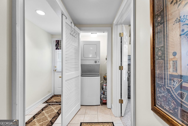 laundry area featuring laundry area, stacked washing maching and dryer, light tile patterned flooring, and baseboards