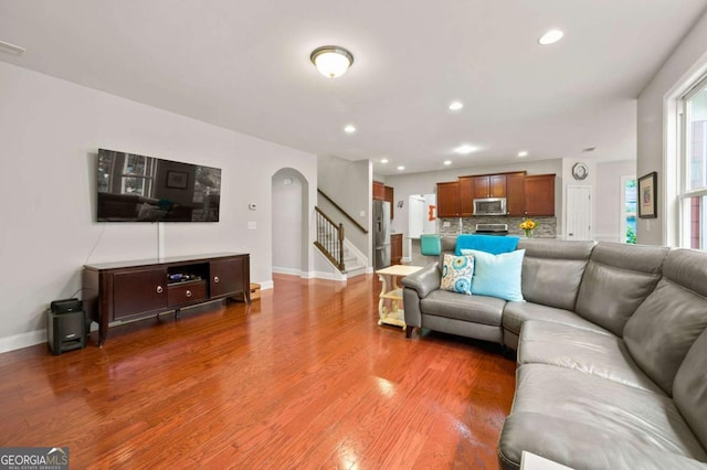 living room with arched walkways, recessed lighting, light wood finished floors, and stairs