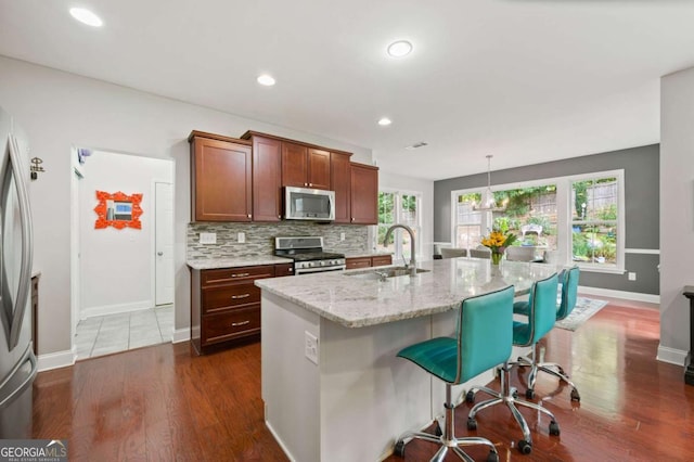 kitchen featuring stainless steel appliances, a sink, a kitchen breakfast bar, decorative backsplash, and light stone countertops