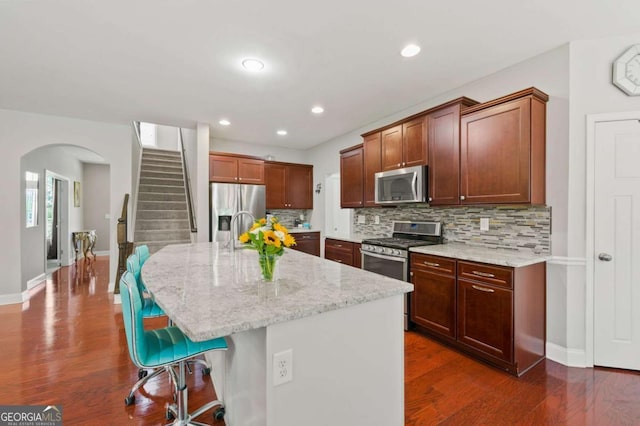 kitchen featuring stainless steel appliances, a breakfast bar area, dark wood finished floors, and decorative backsplash