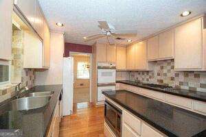 kitchen featuring white appliances, a ceiling fan, dark countertops, light wood-type flooring, and a sink