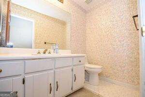 bathroom featuring toilet, wallpapered walls, and vanity