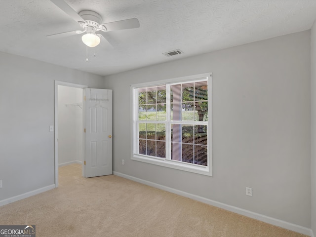 unfurnished bedroom featuring baseboards, visible vents, a walk in closet, a textured ceiling, and carpet floors