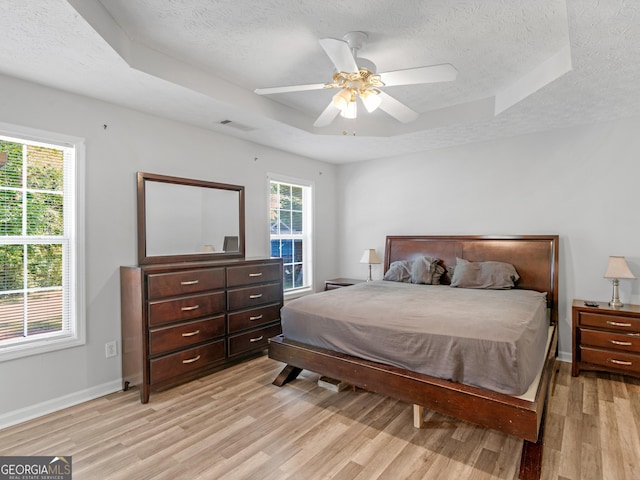 bedroom featuring light wood-type flooring, multiple windows, and a raised ceiling