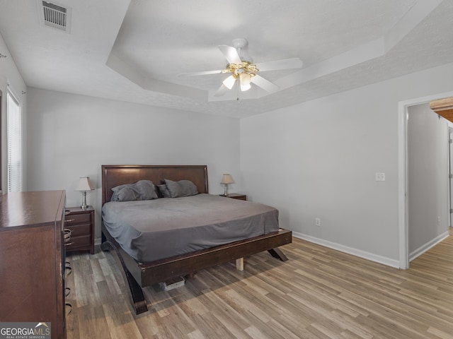 bedroom with light wood finished floors, baseboards, visible vents, and a raised ceiling