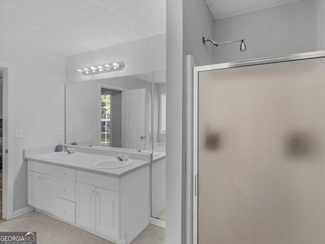 bathroom featuring double vanity, a shower stall, a textured ceiling, and a sink