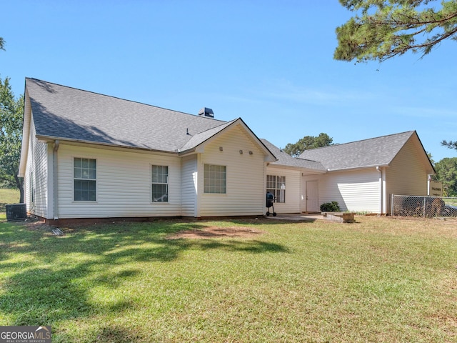 rear view of house featuring central AC, a yard, fence, and roof with shingles