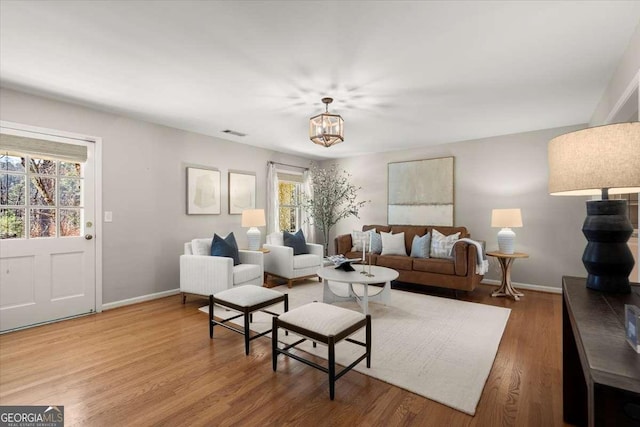 living area with a chandelier, visible vents, baseboards, and wood finished floors