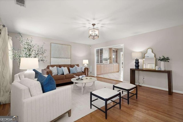 living area featuring a notable chandelier, baseboards, visible vents, and wood finished floors