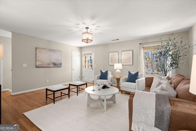 living room with an inviting chandelier, wood finished floors, visible vents, and baseboards